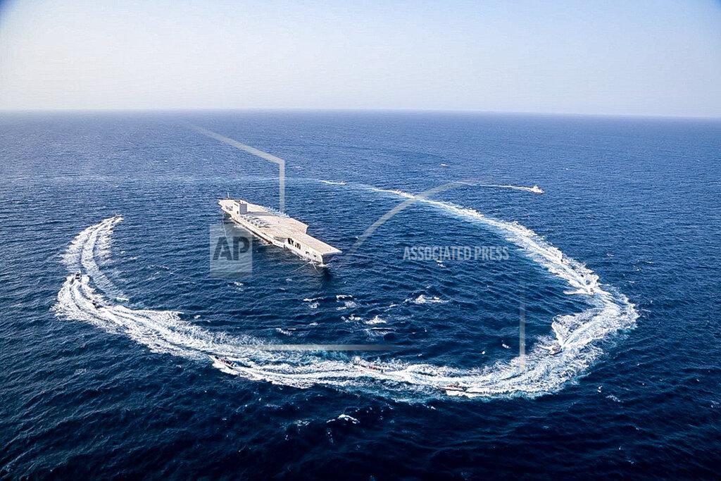 Uncredited In this photo released Tuesday, July 28, 2020, by Sepahnews, Revolutionary Guard's speed boats circle around a replica aircraft carrier during a military exercise. Iran’s paramilitary Revolutionary Guard fired a missile from a helicopter targeting the mock-up aircraft carrier in the strategic Strait of Hormuz according to footage aired on state television on Tuesday. Iranian commandos also fast-roped down from a helicopter onto the replica in the footage from the exercise called “Great Prophet 14.” The drill appears aimed at threatening the U.S. amid tensions between Tehran and Washington. (Sepahnews via AP)