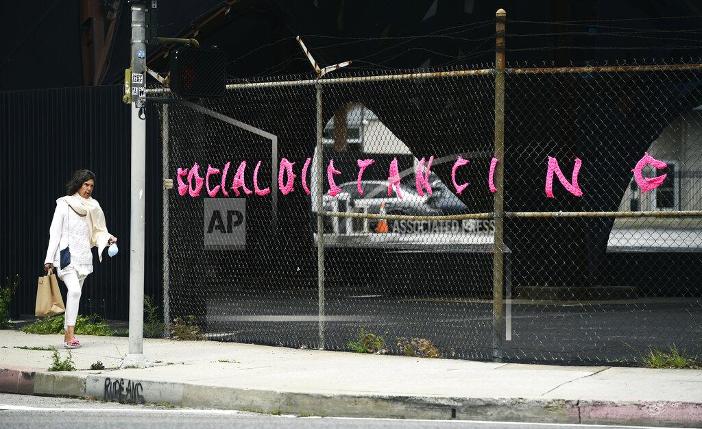 Chris Pizzello A pedestrian walks by a "Social Distancing" message on a fence, made out of yarn by crochet artist London Kaye, as stay-at-home orders continue in California due to the coronavirus outbreak, Friday, April 10, 2020, in the Arts District of Los Angeles. (AP Photo/Chris Pizzello)