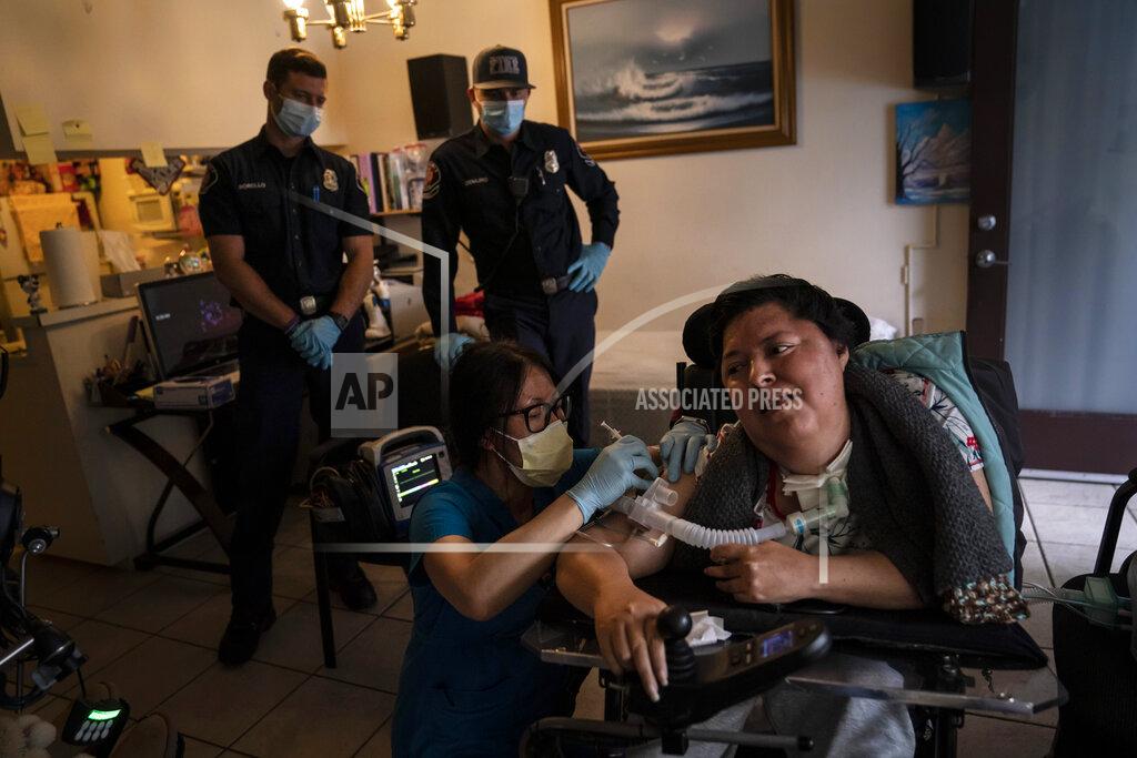 Jae C. Hong Pharmacist Stella Kim, foreground left, administers the second dose of the Pfizer COVID-19 vaccine to Socorro Franco-Martinez, who has muscular dystrophy, in her apartment as Torrance firefighters, Trevor Borello, rear left, and Alessandro Demuro watch Wednesday, May 12, 2021, in Torrance, Calif. Teamed up with the Torrance Fire Department, Torrance Memorial Medical Center started inoculating people at home in March, identifying people through a city hotline, county health department, senior centers and doctor's offices, said Mei Tsai, the pharmacist who coordinates the program. (AP Photo/Jae C. Hong)