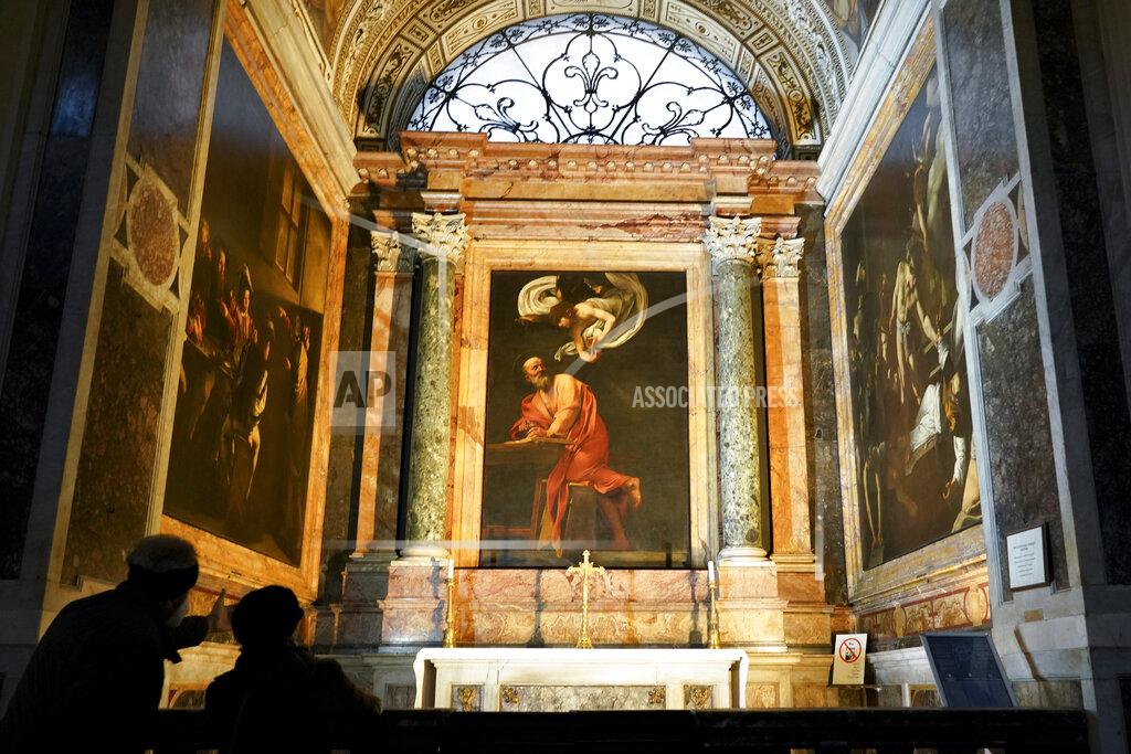 Andrew Medichini Visitors admire a cycle of paintings by 16th century artist Michelangelo Merisi, known as Caravaggio, on the life of St.Matthew, inside the Contarelli chapel of San Luigi dei Francesi Church, in Rome, Friday, Dec. 11, 2020. Like elsewhere in Europe, museums and art galleries in Italy were closed this fall to contain the spread of COVID-19, meaning art lovers must rely on virtual tours to catch a glimpse of the treasures held by famous institutions such as the Uffizi in Florence and the Vatican Museums in Rome. However, some exquisite gems of Italy's cultural heritage remain on display in real life inside the country's churches, some of which have collections of renaissance art and iconography that would be the envy of any museum. (AP Photo/Andrew Medichini)
