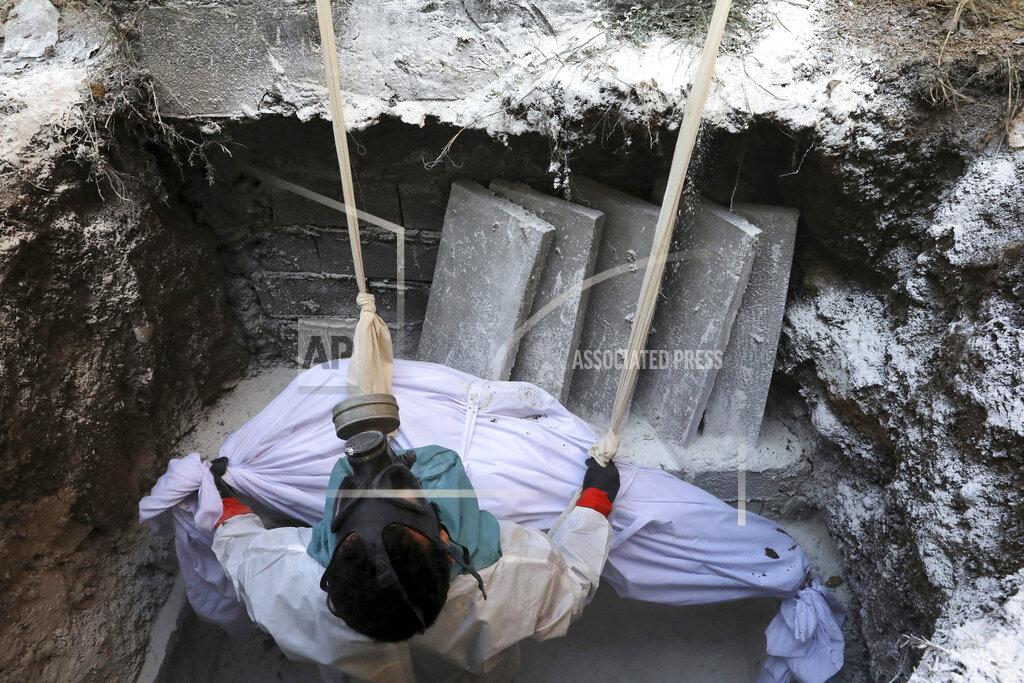 Ebrahim Noroozi A cleric wearing protective clothing lowers the body of a woman who died from COVID-19 into a grave at a cemetery in the outskirts of the city of Ghaemshahr, in northern Iran, Thursday, Dec. 17, 2020. (AP Photo/Ebrahim Noroozi)