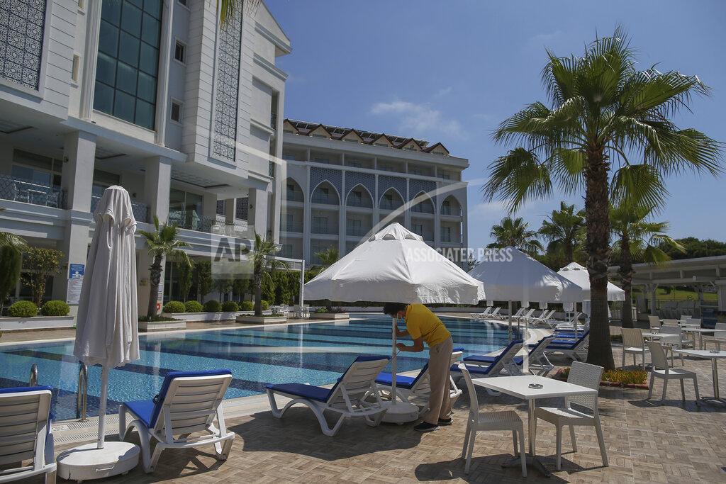 Emrah Gurel A hotel employee wearing a protective face mask opens an umbrella near a swimming pool in Antalya, southern Turkey, Saturday, June 19, 2021. Hotels in Turkey's Antalya region, a destination beloved by holidaymakers, are preparing to finally resume operations as they expect the return of international tourists after months of setbacks caused by the pandemic that halted travel. (AP Photo/Emrah Gurel)