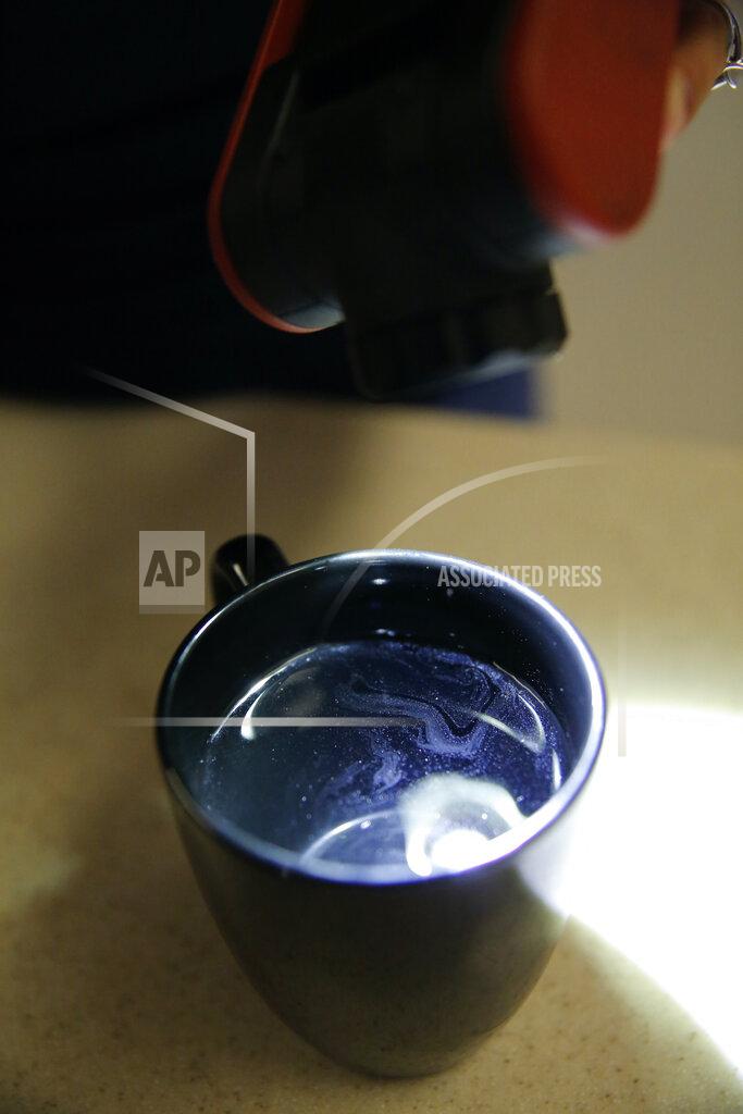 Caleb Jones Lauren Wright, a Navy spouse whose family was sickened by jet fuel in their tap water, shines a light to show a sheen in tap water taken from her kitchen sink in Honolulu, Friday, July 1, 2022. A Navy investigation says shoddy management and human error caused fuel to leak into Pearl Harbor's tap water last year. The leak poisoned thousands of people and forced military families to evacuate their homes for hotels. (AP Photo/Caleb Jones)