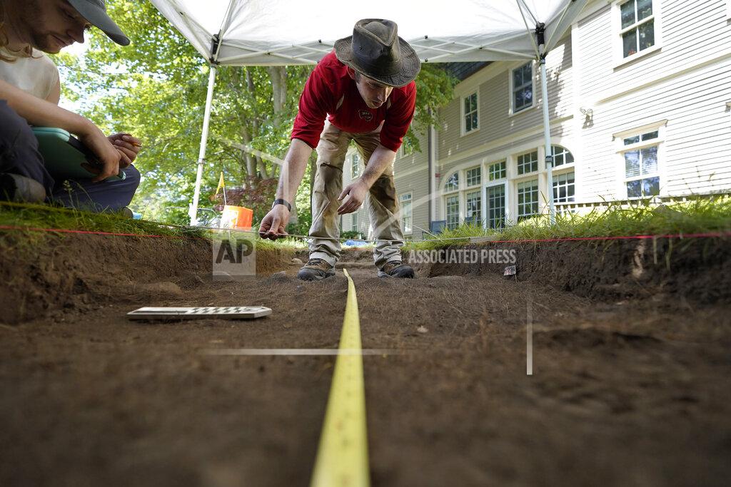 Steven Senne University of Massachusetts Boston graduate students Sean Fairweather, of Watertown, Mass., left, and Alex Patterson, of Quincy, Mass., right, use measuring instruments while mapping an excavation site, Wednesday, June 9, 2021, on Cole's Hill, in Plymouth, Mass. The archaeologists are part of a team excavating the grassy hilltop that overlooks iconic Plymouth Rock one last time before a historical park is built on the site. (AP Photo/Steven Senne)