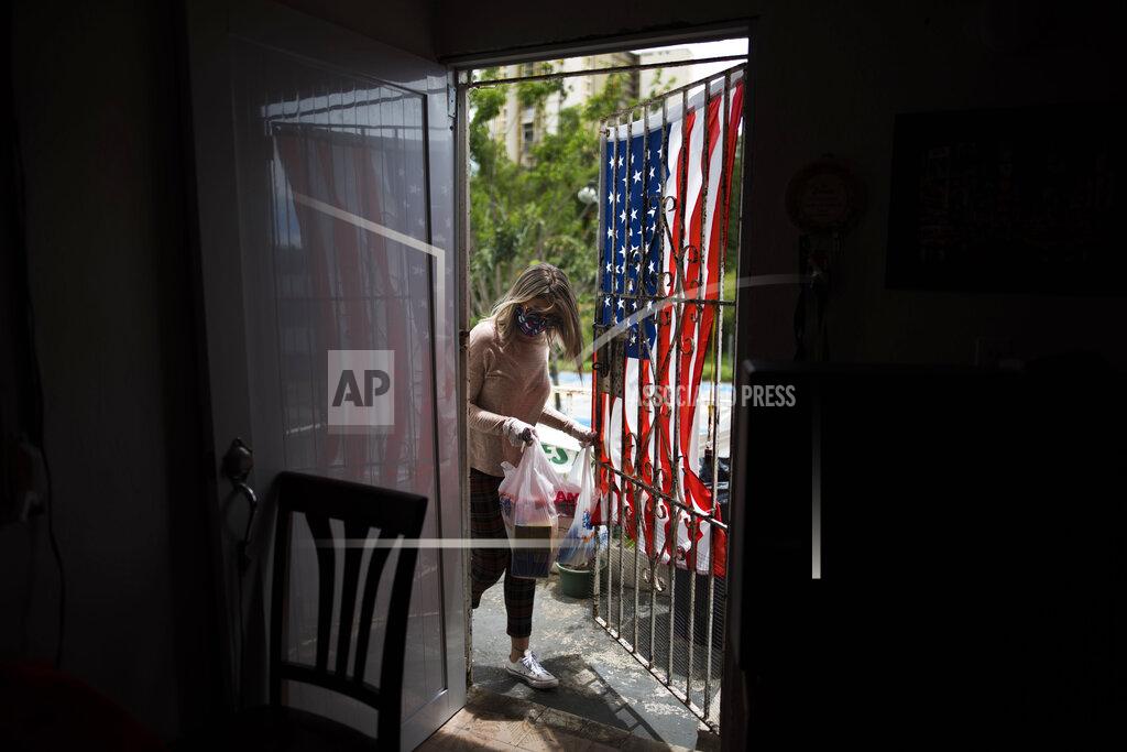 FILE - In this April 29, 2020 file photo, social worker Michelle Valentín, a former teacher, brings food to Angel Ruiz and Ivelisse Rios, a couple who are having a hard time feeding their two children while schools are closed to help contain the spread of the new coronavirus in San Juan, Puerto Rico. On Thursday, June 11, a judge has given Puerto Rico’s education secretary 24 hours to open all school cafeterias in the U.S. territory or face arrest as impoverished students struggle to obtain free meals amid the pandemic. (AP Photo/Carlos Giusti, File)