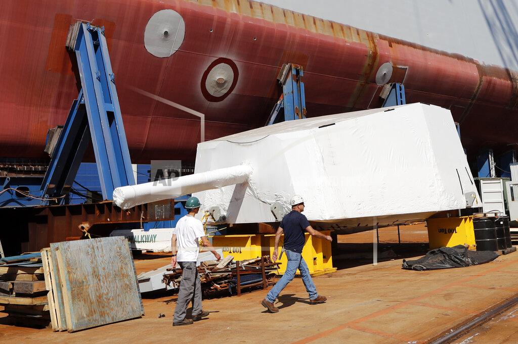 Robert F. Bukaty In this Wednesday, Aug. 29, 2018 file photo, workers walk by the Advanced Gun System, covered in shrink wrap, alongside a Zumwalt-class destroyer being built in the shipyard at Bath Iron Works in Bath, Maine. The return of shipbuilders after a nine-week strike, which officially ended Aug. 23, 2020, is going smoothly at Bath Iron Works and the union and company already have begun meeting to get back on track. (AP Photo/Robert F. Bukaty)