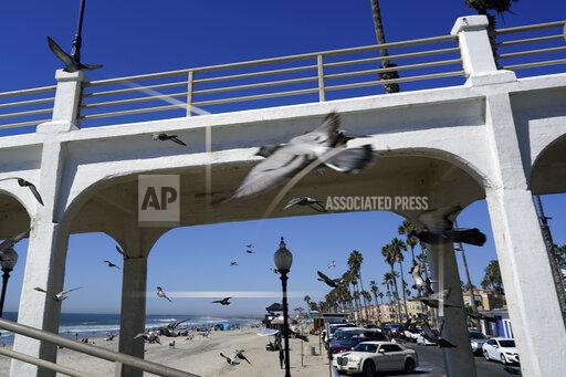 Birds fly past a bridge connecting the Oceanside pier to Pacific Street Friday, Oct. 15, 2021, in Oceanside, Calif. The iconic bridge is deteriorating because the city lacks the money for a roughly $25 million rehabilitation. One reason the project has slowed while projects in other cities are moving ahead revolves around the American Rescue Plan — the sweeping COVID-19 relief law championed by President Joe Biden and congressional Democrats that is pumping billions of dollars to states and local governments. (AP Photo/Gregory Bull)