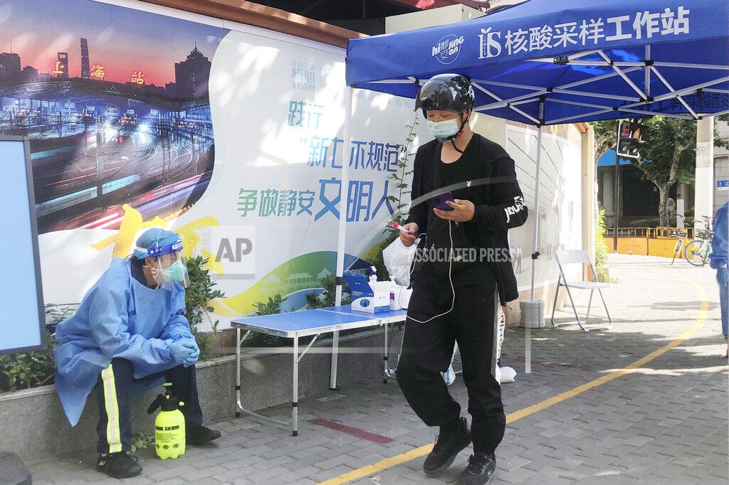 Chen Si A resident walks past a worker at a sample collection center for mass COVID testing in Shanghai, China, Sunday, May 22, 2022. Numerous residential compounds in Beijing have restricted movement in and out, although conditions remain far less severe than in Shanghai, where millions of citizens have been under varying degrees of lockdown for two months. (AP Photo/Chen Si)
