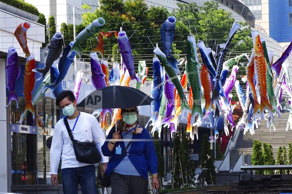 Eugene Hoshiko People with face masks to help stop the spread of the coronavirus walk under colorful carp streamers in Tokyo Saturday, May 2, 2020. Prime Minister Shinzo Abe said that he planned to extend a state of emergency beyond the scheduled end of May 6 because infections are spreading and hospitals are overburdened. The streamers were hung to mark Children's Day on May 5, wishing children's healthy growth like carp that can swim up a waterfall. (AP Photo/Eugene Hoshiko)