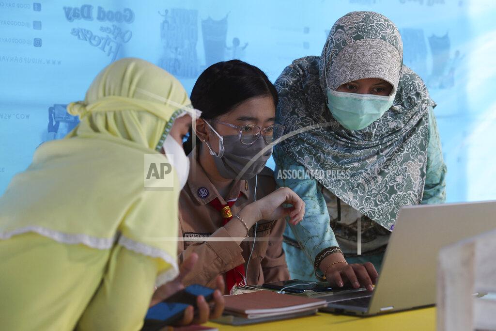 A mother, right, and her daughter, center, wear face masks to help curb the spread of the new coronavirus as they use free wifi to access an online lesson inside a temporary tent in Jakarta, Indonesia, Wednesday, Aug. 12, 2020. In some areas of the country, students are still yet to go to school due to the coronavirus. (AP Photo/Achmad Ibrahim)