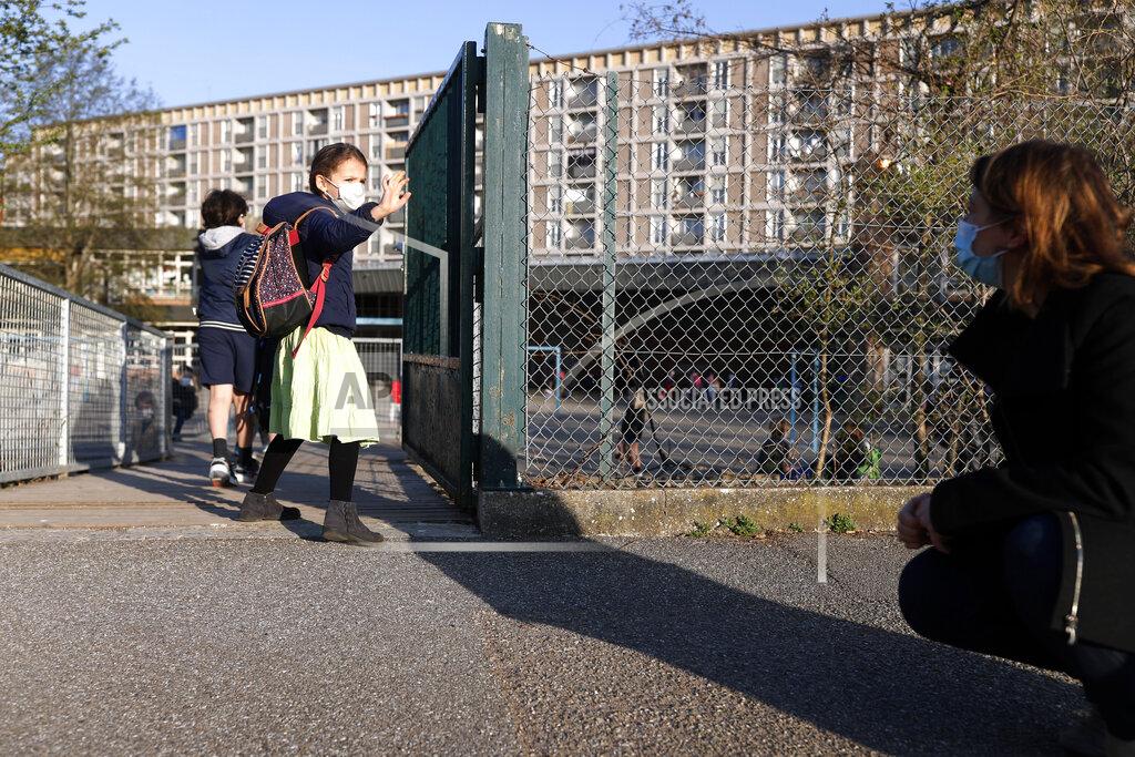 FILE - In this Thursday, April 1, 2021 file photo, Emma Woodroof waves goodbye to her mother Julie as she enters her school in Strasbourg, eastern France. Children, parents and teachers are battling with connection problems across France after an abrupt nationwide switch to online learning saturated networks and embarrassed the government. Paris prosecutors opened an investigation into possible hacking into key systems, the prosecutor’s office said Wednesday, April 7. (AP Photo/Jean-Francois Badias)