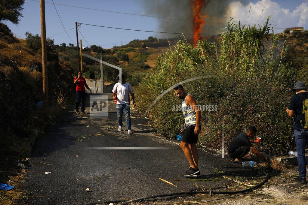 Migrants try to extinguish a small fire in a field near Mytilene town, on the northeastern island of Lesbos, Greece, Saturday, Sept. 12, 2020. Thousands of asylum-seekers spent a fourth night sleeping in the open on the Greek island of Lesbos, after successive fires destroyed the notoriously overcrowded Moria camp during a coronavirus lockdown. (AP Photo/Petros Giannakouris)