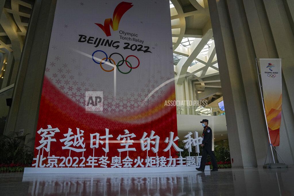 A security guard wearing a face mask to help curb the spread of the coronavirus patrols past a Beijing 2022 Winter Olympic Games decoration for a welcome ceremony for the Frame of Olympic Winter Games Beijing 2022, held at the Olympic Tower in Beijing, Wednesday, Oct. 20, 2021. A welcome ceremony for the Olympic flame was held in Beijing on Wednesday morning after it arrived at the Chinese capital from Greece. While the flame will be put on display over the next few months, organizers said a three-day torch relay is scheduled starting Feb. 2 with around 1200 torchbearers in Beijing, Yanqing and Zhangjiakou. (AP Photo/Andy Wong)