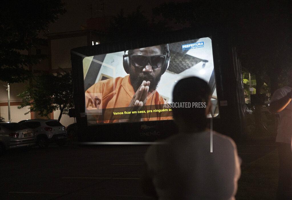A woman watches a short film on a giant screen in Rio de Janeiro, Brazil, Wednesday, May 13, 2020. Cinema from the windows is the name of a Rio City Hall initiative to bring the movie theater to people in quarantine at home due to the coronavirus pandemic. (AP Photo/Silvia Izquierdo)