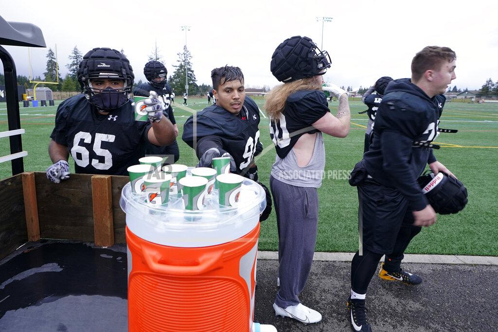 Ted S. Warren Pacific Lutheran football players help themselves to individual cups of water during practice Tuesday, Feb. 2, 2021, in Tacoma, Wash. The cups have replaced shared squirt bottles as a measure attempting to prevent the spread of COVID-19. For all the attention heaped on the FBS level of college football last fall as it tried to play, it will not be the only college football during the 2020-21 sports calendar as a handful of NCAA Division III and NAIA programs begin some form of a winter/spring season Saturday, Feb. 6. (AP Photo/Ted S. Warren)