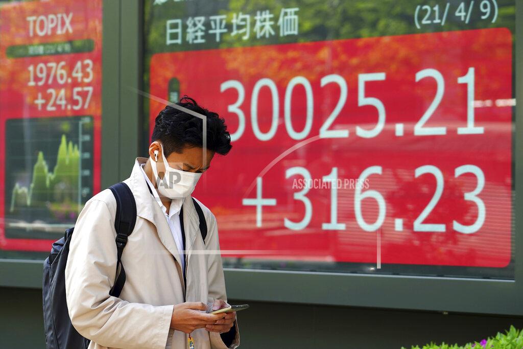 A man wearing a protective mask walks in front of an electronic stock board showing Japan's Nikkei 225 index at a securities firm in Tokyo Friday, April 9, 2021. (AP Photo/Eugene Hoshiko)
