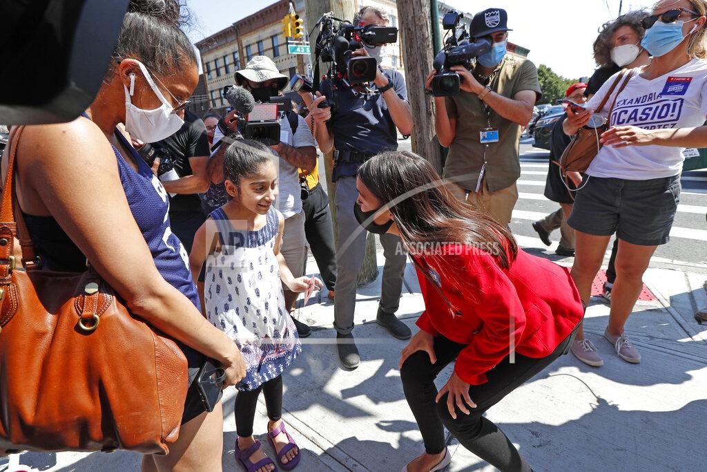 Kathy Willens U.S. Rep. Alexandria Ocasio-Cortez, D, New York, center right, kneels to speak to six year-old Aradhya Vaid, as Vaid's mother Upkar Chana looks on, as the first-term congresswoman greeted voters in Astoria, Queens, Tuesday, June 23, 2020, on primary election day in New York. (AP Photo/Kathy Willens)