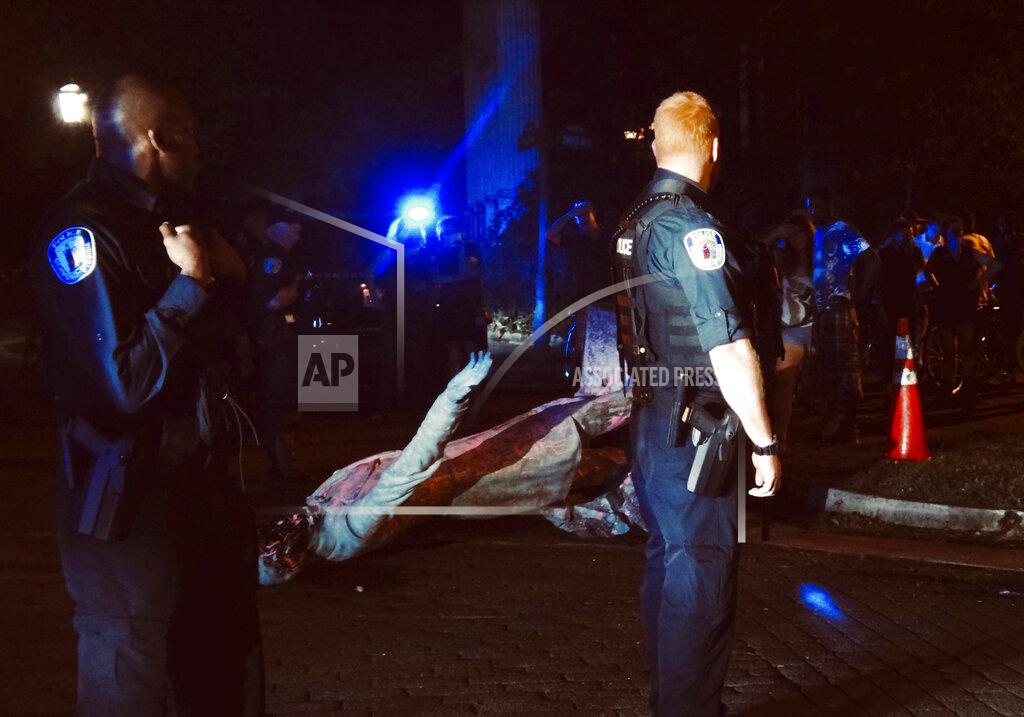 In this photo provided by @thicketoftrash, a police officer looks toward the toppled statue of Confederate President Jefferson Davis along Monument Avenue, Wednesday night, June 10, 2020, in Richmond, Va. (@thicketoftrash via AP)