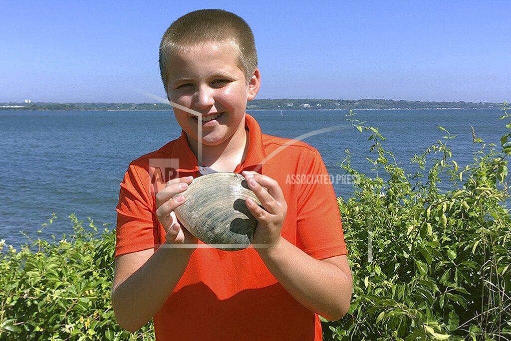 In this Tuesday, July, 28, 2020, photo provided by the University of Rhode Island, Cooper Monaco holds the large quahog he found Monday while clamming with his grandfather in Westerly, R.I. The quahog is more than five inches across and weighing more than two pounds, and is among the largest ever harvested in the state. The mollusk was donated to the University of Rhode Island's Marine Science Research Facility. (Todd McLeish/University of Rhode Island via AP)