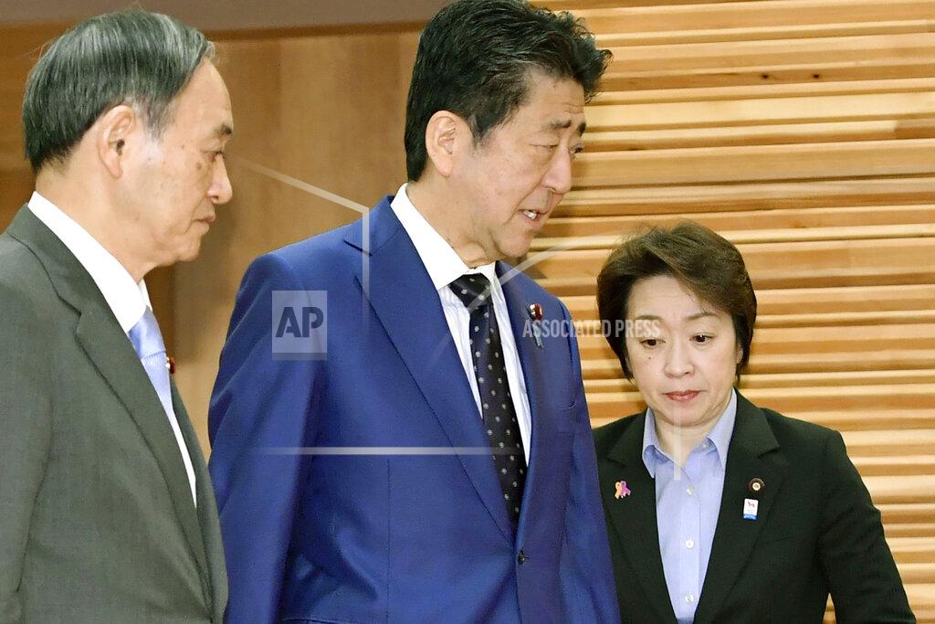 Yoshitaka Sugawara Japanese Prime Minister Shinzo Abe, center, walks past Olympic Minister Seiko Hashimoto, right, to attend a cabinet meeting at his official residence in Tokyo Tuesday, March 24, 2020. Hashimoto said the global pandemic of coronavirus infections should end before Japan can proceed with hosting the Tokyo Olympic Games, after the meeting. Tokyo's organizers and International Olympic Committee are discussing a possible postponement and other scenarios. Abe and IOC President Thomas Bach are expected to hold telephone talks later Tuesday. At left is Chief Cabinet Secretary Yoshihide Suga. (Yoshitaka Sugawara/Kyodo News via AP)