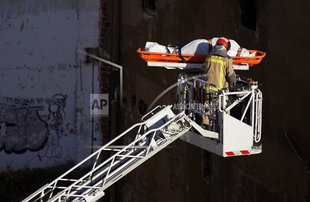 Joan Mateu Firefighters load the body of a dead person into a crane after a fire on a building in Badalona, Barcelona, Spain, Thursday, Dec. 10, 2020. Authorities in northeastern Spain say a fire has raged through an abandoned building occupied by squatters in the city of Badalona, injuring at least 17 people, including two in critical condition. Firefighters say they rescued around 30 people from windows as the building burned late Wednesday. (AP Photo/Joan Mateu)