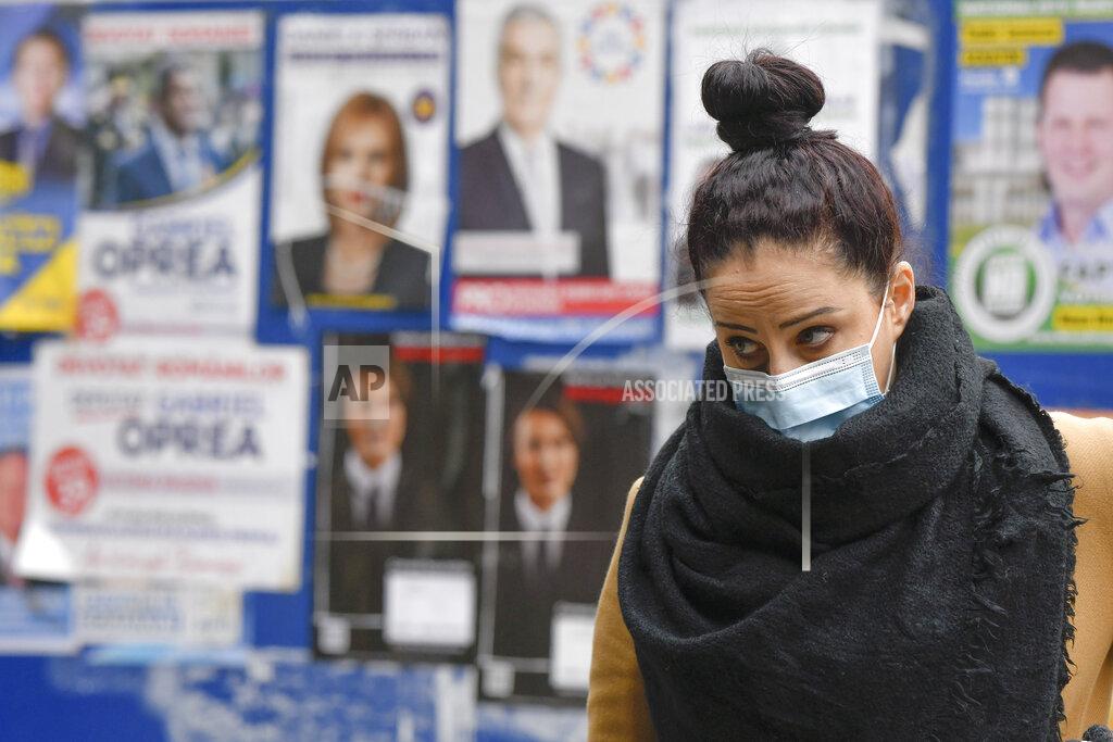 Andreea Alexandru A woman wearing a mask for protection against the COVID-19 infection walks by electoral posters in Bucharest, Romania, Thursday, Dec. 3, 2020. Romania will hold parliamentary elections on Sunday Dec. 6. (AP Photo/Andreea Alexandru)