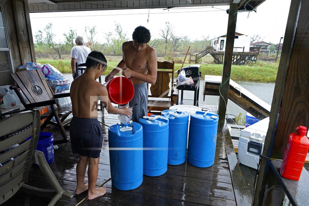 Gerald Herbert Terren Dardar, 17, and Dayton Verdin, 14, left, pour barrels of rainwater they collected from Tropical Storm Nicholas, in the aftermath of Hurricane Ida in Pointe-aux-Chenes, La., Tuesday, Sept. 14, 2021. They have had no running water since the hurricane, and collected 140 gallons of rainwater in two hours from the tropical storm, which they filter and pump into their house for showers. (AP Photo/Gerald Herbert)