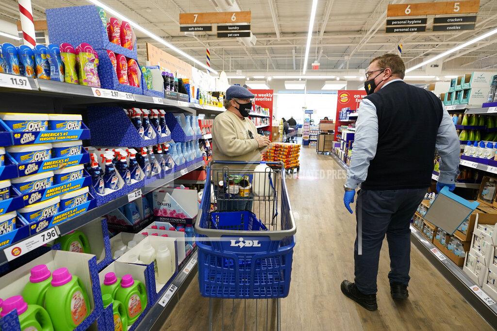 Kathy Willens In this Thursday, Feb. 4, 2021 photo, a customer asks Lidl employee Joseph Lupo, right, for help finding a product inside the Lidl grocery market in Lake Grove, N.Y. Lupo received his first dose of the coronavirus vaccination earlier in the day. The German grocery chain is offering $200 in extra pay to employees willing to get vaccinated against COVID-19. Lupo, a Lidl supervisor who fell ill with the virus in March, was elated to get his first vaccine dose. "I never ever want to get COVID again, or see anybody else get it," said Lupo, 59. (AP Photo/Kathy Willens)