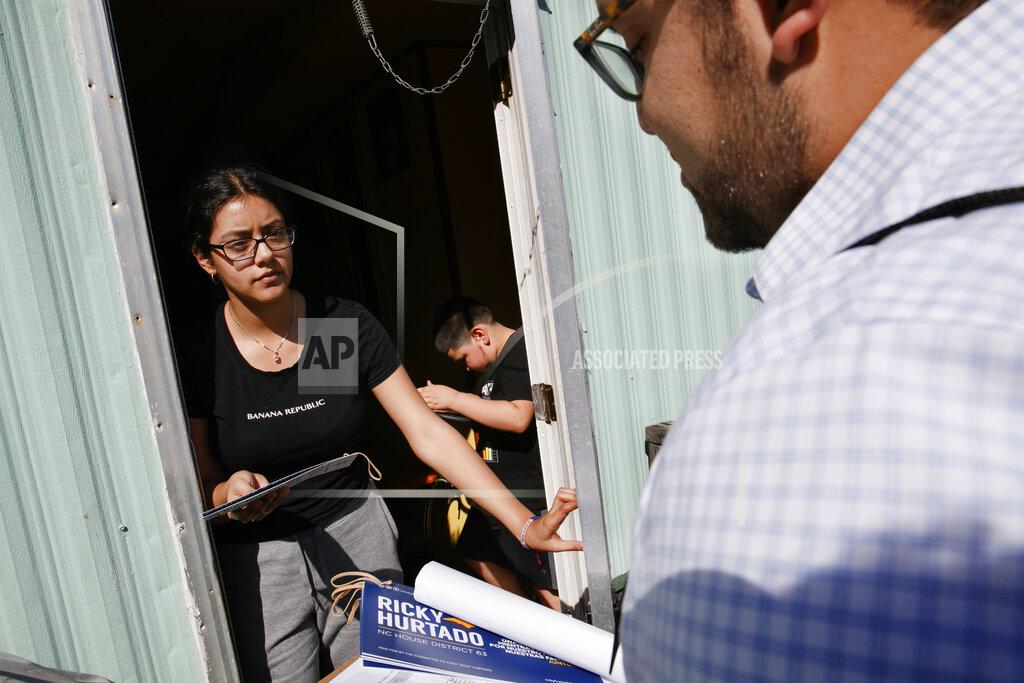 Evelyn Lara, 19, with her brother Iker, 7, opens the door as Ricky Hurtado, a Democratic candidate for the North Carolina state house, canvasses voters in a largely Latino trailer community, in Burlington, N.C., Sunday, March 8, 2020. (AP Photo/Jacquelyn Martin)