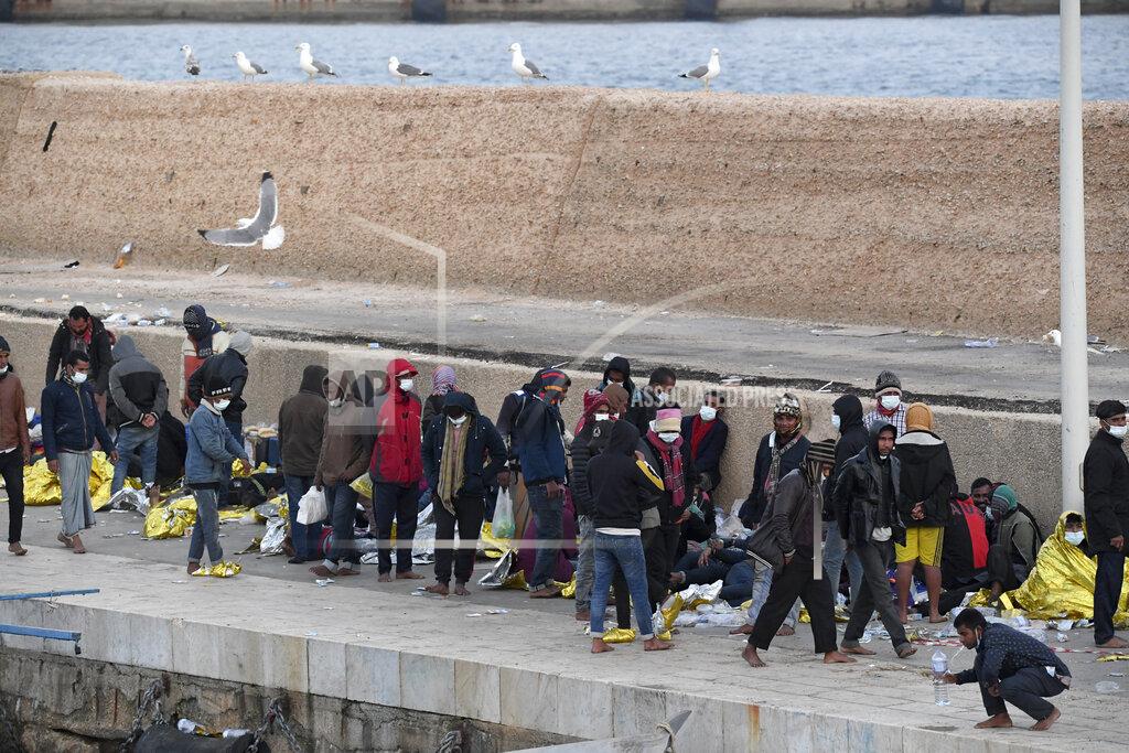 Salvatore Cavalli Migrants stand on a pier after arriving on the Sicilian island of Lampedusa, southern Italy, Monday, May 10, 2021. Several hundred more migrants reached the tiny Italian island before dawn on Monday, swelling to past 2,100 the number of arrivals in around 24 hours and fueling calls from across the political spectrum for the Italian government to strengthen its migration policies. (AP Photo/Salvatore Cavalli)