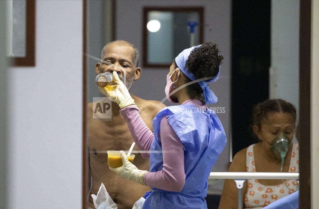 Photographed through a door from outside the José Gregorio Hernández Hospital, Mirley Avila feeds her father Miguel Avila inside the COVID-19 wing in the Catia neighborhood of Caracas, Venezuela, Saturday, Oct. 10, 2020, on a day when there weren't enough nurses so they let her in to feed him, change his sheets and undergarments. According to Caracas Nurses College President Ana Rosario Contreras, a 2018 survey by the organization found that at least 6,000 nurses have abandoned Venezuela and that the number has grown since. (AP Photo/Ariana Cubillos)