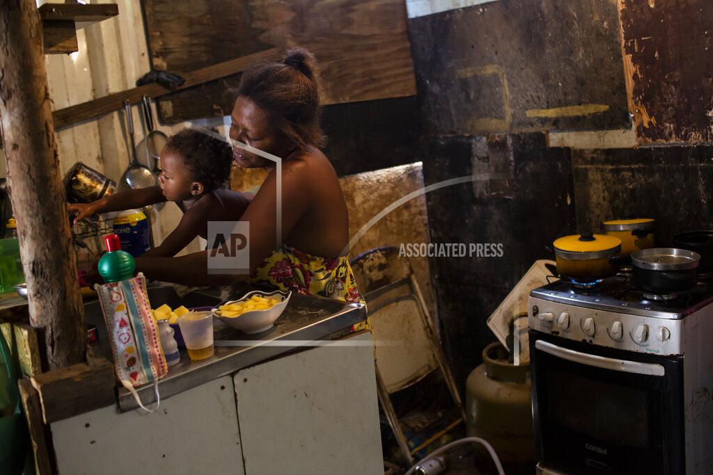 Bruna Prado FILE - In this April 18, 2021 file photo, Debora Estanislau, who made her living as a domestic worker before the new coronavirus pandemic hit, holds her one-year-old daughter Ana Beatriz as she cooks at home where she lives with her four children in the Cidade de Deus favela in Rio de Janeiro, Brazil. Limited and reduced welfare payments is leaving vulnerable Brazilians exposed to soaring food prices and a still-worsening job market. (AP Photo/Bruna Prado, File)