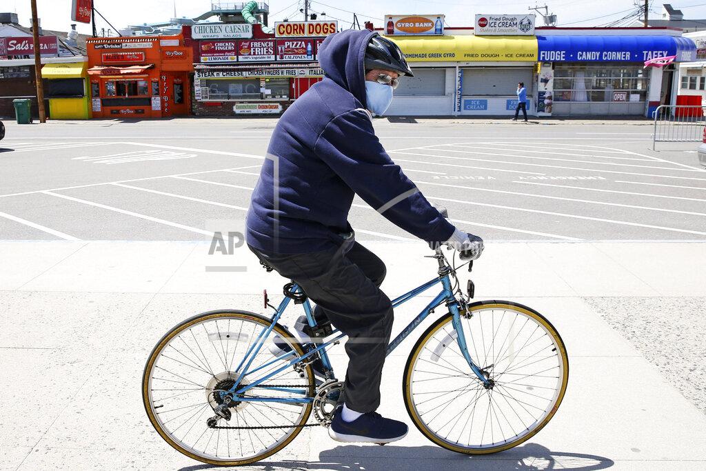 A man wearing a protective mask and gloves cycles past the Boardwalk across from the Hampton Beach State Park in Hampton, N.H., Tuesday, May 19, 2020. Beaches in New Hampshire have been closed since March by state order due to the COVID-19 virus outbreak. (AP Photo/Charles Krupa)