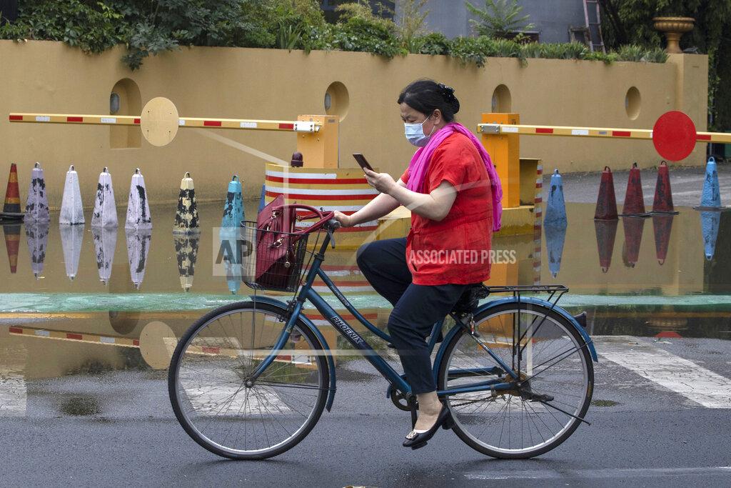 Ng Han Guan A woman wearing a mask to curb the spread of the coronavirus cycle along a street after a downpour in Beijing on Thursday, June 25, 2020. In China, where the virus first appeared late last year, an outbreak in Beijing appeared to have been brought under control. China reporting more than a dozen of newly confirmed cases nationwide amid mass testing in the capital. (AP Photo/Ng Han Guan)