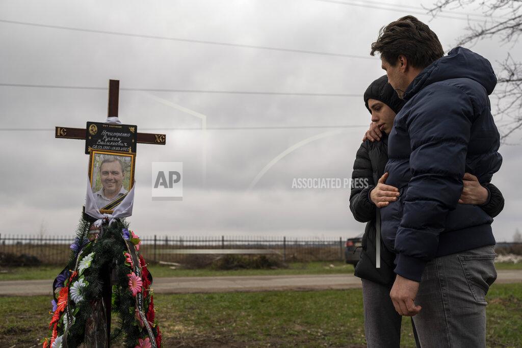 Petros Giannakouris Yura Nechyporenko, 15, hugs his uncle Andriy Nechyporenko above the grave of his father Ruslan Nechyporenko at the cemetery in Bucha, on the outskirts of Kyiv, Ukraine, on Thursday, April 21, 2022. The teen survived an execution attempt by Russian soldiers while his father was killed, and now his family seeks justice. (AP Photo/Petros Giannakouris)