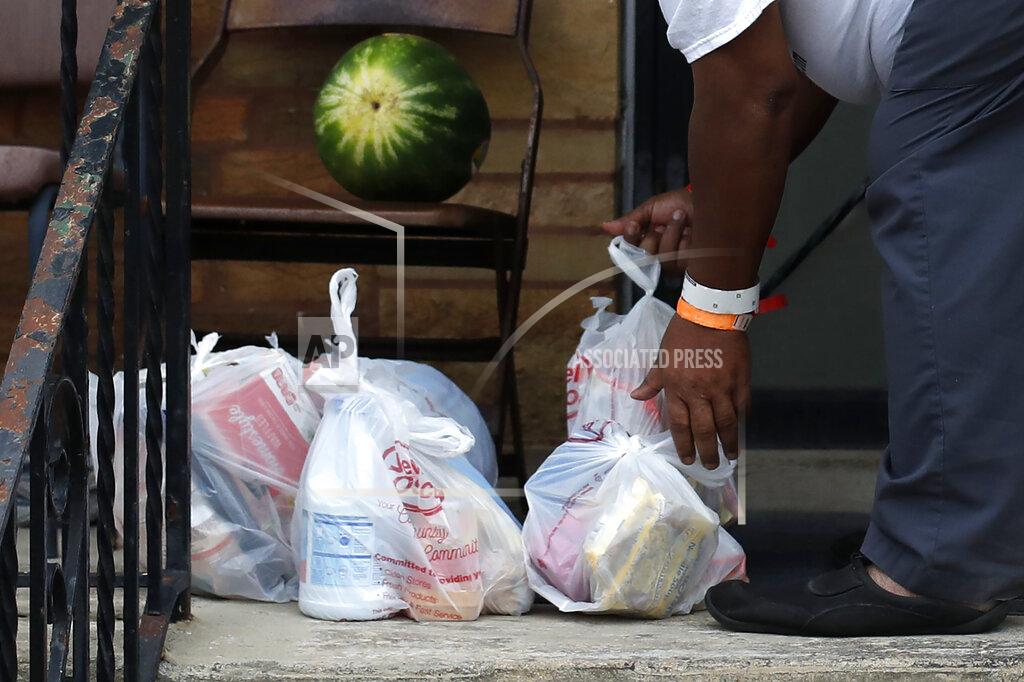 Charles Rex Arbogast Anthony Travis, who has recovered from COVID-19 and lives with his sister and an adult daughter, gathers a surprise anonymous delivery of groceries on the porch of his Riverdale, Ill., home on Thursday, April 23, 2020. Travis, who's diabetic, has high blood pressure and is a cancer survivor, must self isolate within the home as a matter of taking care of one another. (AP Photo/Charles Rex Arbogast)