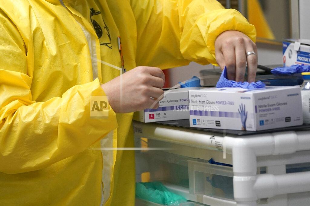 FILE - In this July 6, 2020, file photo, a medical student reaches for some gloves while working inside the Coronavirus Unit in a Houston hospital. Hospital data related to the coronavirus pandemic in the U.S. will now be collected by a private technology firm, rather than the Centers for Disease Control and Prevention — a move the Trump administration says will speed up reporting but one that concerns some public health leaders. (AP Photo/David J. Phillip, File)
