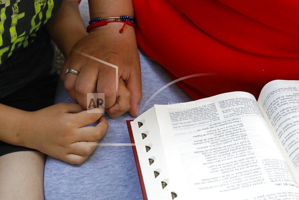 Shafkat Anowar Eugenia Rodriguez holds the hand of her youngest son, Aaron, 6, while reading from the Bible in her house, Friday, July 2, 2021, in Chicago's Little Village neighborhood. Rodriguez hasn't been eligible for insurance coverage after overstaying a visitor visa from Mexico. She used to wake up every two or three hours at night to check on her mother. Since getting health insurance through the Illinois program, her mother has all the medications she needs. (AP Photo/Shafkat Anowar)