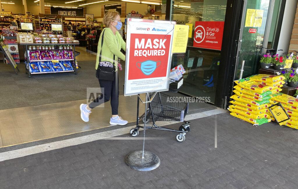 David Zalubowski In this Wednesday, May 19, 2021, photograph, a shopper pushes her basket filled with purchases past a sign advising the need to wear face masks while in a Safeway grocery store in Aurora, Colo. Retail workers who are fully vaccinated are concerned as retailers loosen mask-wearing restrictions in their establishments. (AP Photo/David Zalubowski)