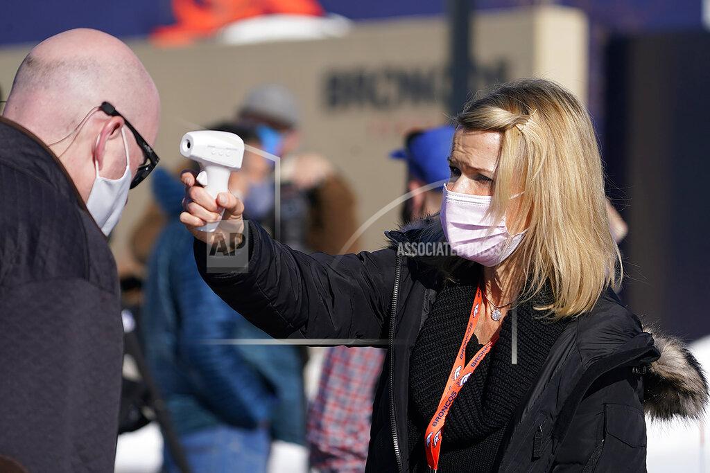 Rachel Deets, right, special events assistant for the Denver Broncos, uses a thermometer to take the temperature of beat writer Ryan O'Halloran before he can watch the team take part in drills during an NFL football practice at the team's headquarters Wednesday, Nov. 25, 2020, in Englewood, Colo. (AP Photo/David Zalubowski)