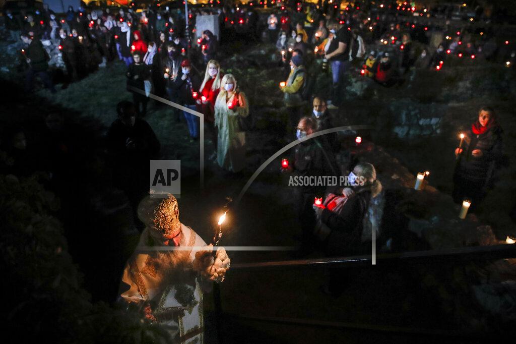 Vadim Ghirda FILE - In this Wednesday, May 27 2020, file picture Romanian Orthodox Archbishop Teodosie holds a candle as orthodox worshipers, a few wearing masks for protection against the COVID-19 virus, stand around the remains of buildings, the oldest from the sixth century BC, during a religious service in the Black Sea port of Constanta, Romania. As Romania battles against a surge of COVID-19 infections authorities announced on Thursday March 25, 2021, that Easter celebrations in the deeply Christian country will physically go ahead this year. (AP Photo/Vadim Ghirda, File)