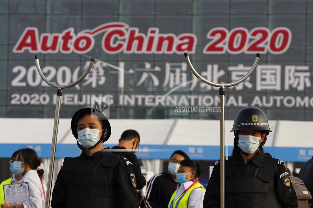 Ng Han Guan Security guards wearing masks and armed with restrainers stand guard at the entrance to the Auto China 2020 show in Beijing, China on Saturday, Sept. 26, 2020. The auto show, the first major in-person sales event for any industry since the coronavirus pandemic began, opens Saturday in a sign the ruling Communist Party is confident China has contained the disease. Still, automakers face intensive anti-virus controls including quarantines for visitors from abroad and curbs on crowd sizes at an event that usually is packed shoulder-to-shoulder with spectators. (AP Photo/Ng Han Guan)