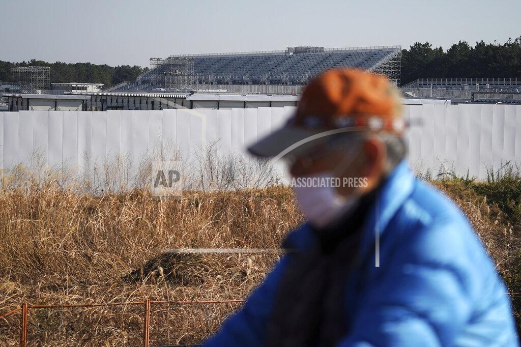 Eugene Hoshiko A man rides a bicycle past Canoe Slalom Course, one of the venues of Tokyo 2020 Olympic and Paralympic games, in Tokyo Thursday, Jan. 21, 2021. The postponed Tokyo Olympics are to open in just six months. Local organizers and the International Olympic Committee say they will go ahead on July 23. But it’s still unclear how this will happen with virus cases surging in Tokyo and elsewhere around the globe. (AP Photo/Eugene Hoshiko)