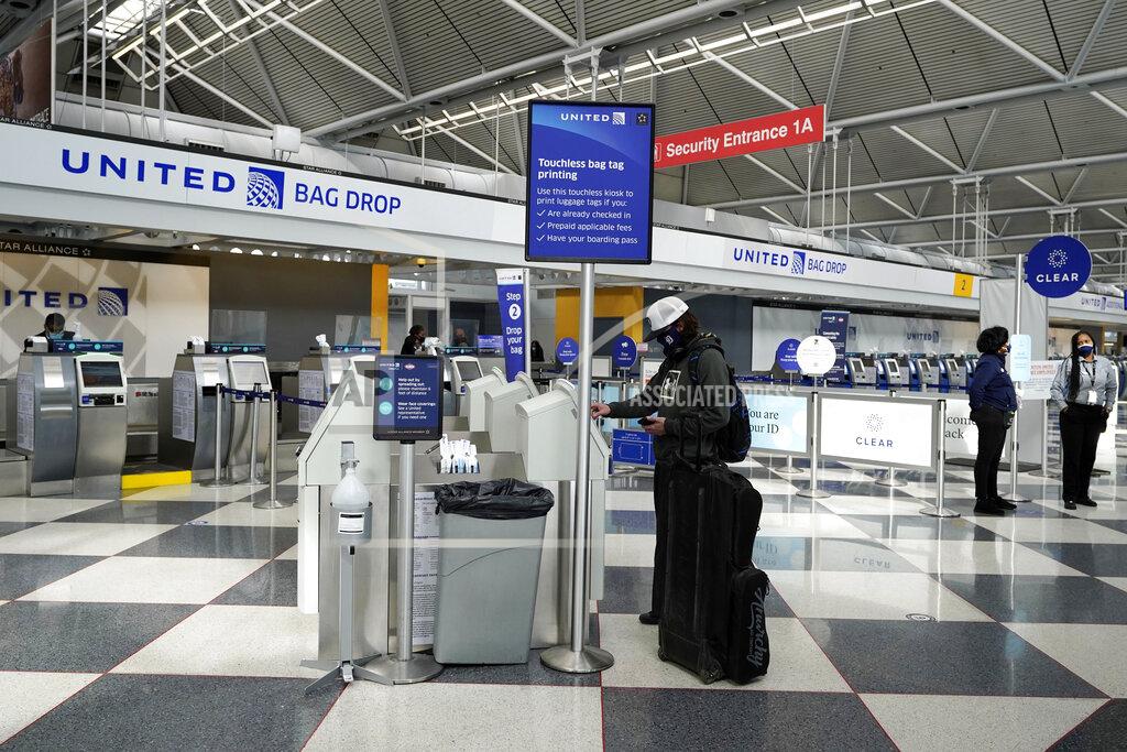 A traveler wears a mask as he checks his flight status information at United Airlines self ticket counter at O'Hare International Airport in Chicago, Wednesday, Oct. 14, 2020. United Airlines, which furloughed 13,000 employees this month, is expected to report a large third-quarter loss as the coronavirus pandemic continues to batter air travel. (AP Photo/Nam Y. Huh)