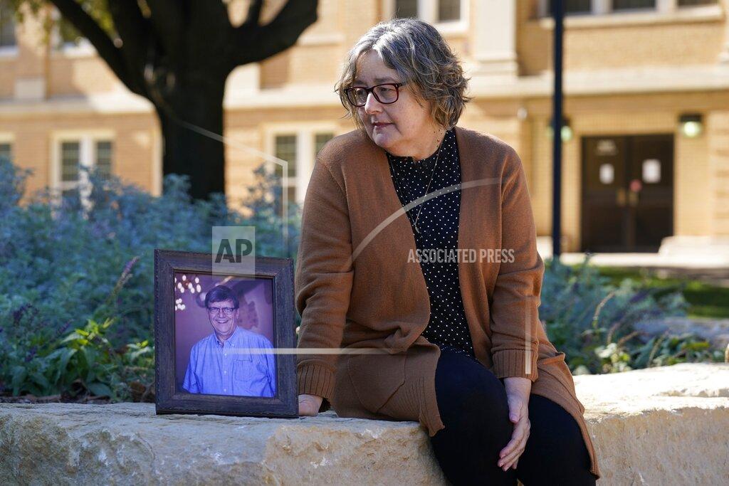Tony Gutierrez Debbie Riggs poses for a photo, sitting by a portrait of her late husband, Mark Riggs on the campus of Abilene Christian University, Wednesday, Dec. 16, 2020, in Abilene, Texas. Mark, who was a professor at the school, passed away of COVID-19 last Monday. Pressure is intensifying on governors who haven’t issued mandates as new coronavirus cases and deaths soar before Christmas. But the debate over mandates and lockdowns often drowns out the reality of whether the restrictions enacted are actually enforced. In the rugged West Texas town of Abilene, the number of deaths has doubled over the past month and intensive care unit beds have been full for weeks. (AP Photo/Tony Gutierrez)