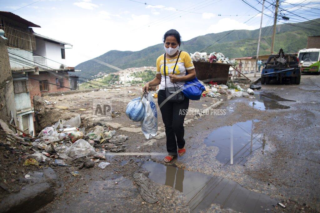 Ariana Cubillos Elena Suazo carries the hospital sheets she replaced for her father, and the protective medical gear she wore to attend him at José Gregorio Hernández Hospital as she walks home in the Catia neighborhood of Caracas, Venezuela, Monday, Sept. 29, 2020. A shortage of doctors and nurses leaves families rushing to fill the void at facilities that treat the poor, to feed them, bathe them and change their bedsheets. (AP Photo/Ariana Cubillos)