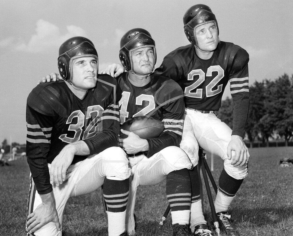 Uncredited FILE - In this Aug. 25, 1948, file photo, veteran quarterback Sid Luckman, center, poses with two newcomers to the Chicago Bears, Johnny Lujack, left, and, Bobby Layne, during preseason football workouts at Collegeville, Ind. Helmets have evolved from the original hard leather of the NFL’s infancy to hard polycarbonate single-piece shells with various amounts of padding and air bladders that served as the primary form of head protection into the beginning of this century. (AP Photo/File)