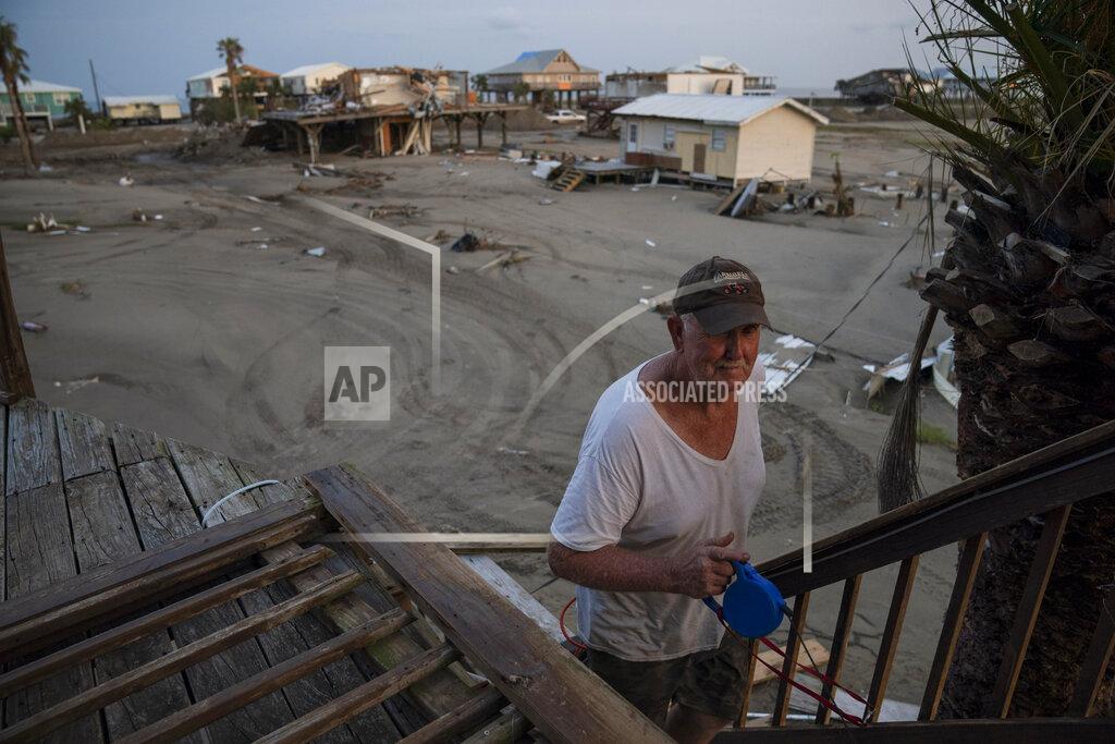 John Locher Kelty Readenour walks up the stairs of his damaged home in the aftermath of Hurricane Ida, Monday, Sept. 6, 2021, in Grand Isle, La. Behind him, sand and debris cover the road. (AP Photo/John Locher)