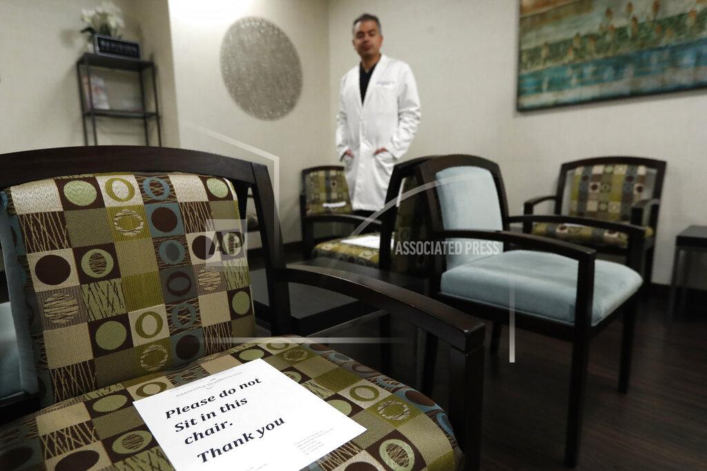 Tony Gutierrez Dermatologist Dr. Seemal Desai poses for a photo in the waiting room of his office in Plano, Texas, Thursday, May 7, 2020. Desai said that they have posted signs on seating that would help patients adhere to social distancing, but on this day in an early afternoon, his office is empty of patients. (AP Photo/Tony Gutierrez)