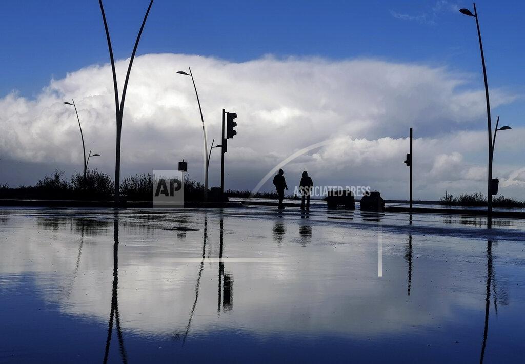 Hassan Ammar Residents walk along the seaside promenade in Beirut, Lebanon, Wednesday, Feb. 17, 2021. A strong storm in Lebanon brought cold temperatures and snow to Lebanon's mountains and heavy rainfall, strong winds on the Lebanese coast. (AP Photo/Hassan Ammar)